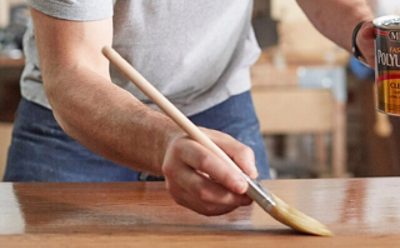 A person staining a table using Minwax polyurethane.